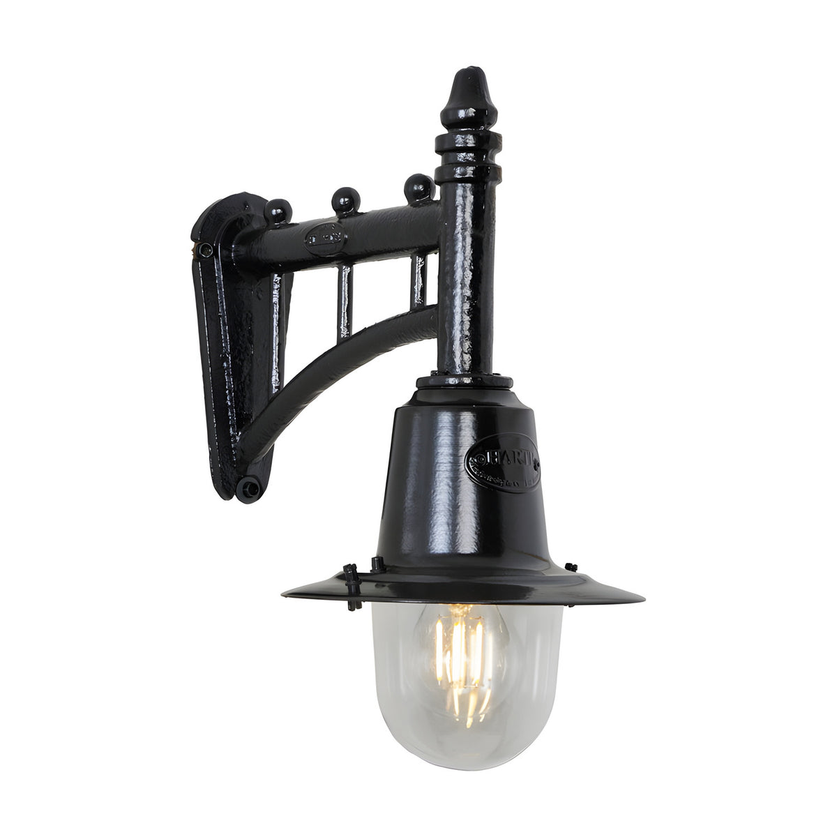 Small railway style wall lantern in black, with a trussed cast arm, spun metal shade and clear glass dome housing an exposed filament bulb, shown on a plain white background.
