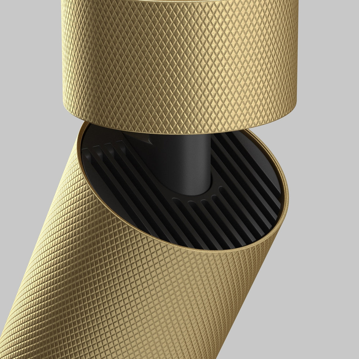 A close-up of the Artisan Single Spotlight - Matte Gold reveals a gold textured cylinder with a diamond pattern intersecting a sleek black cylinder adorned with parallel grooves, exuding contemporary luxury against a plain gray background.