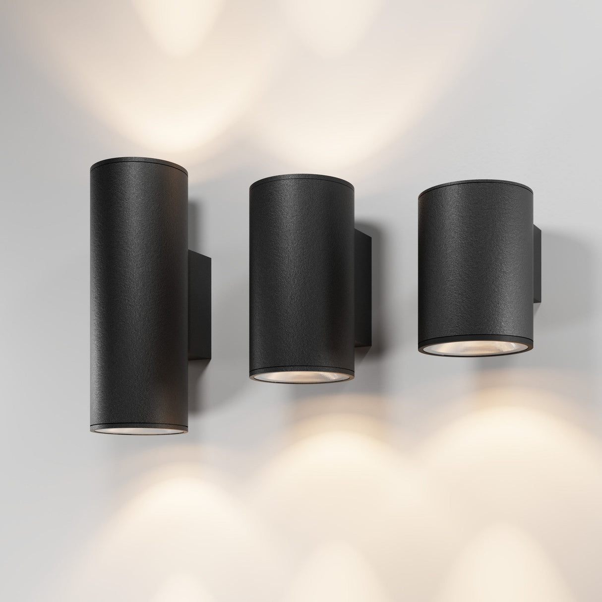 Three Shim Outdoor Wall Lights 10W 3000K in graphite are mounted on a light-colored wall, casting soft circular light patterns up and down. These fixtures boast an IP65 rating for durability in any weather.
