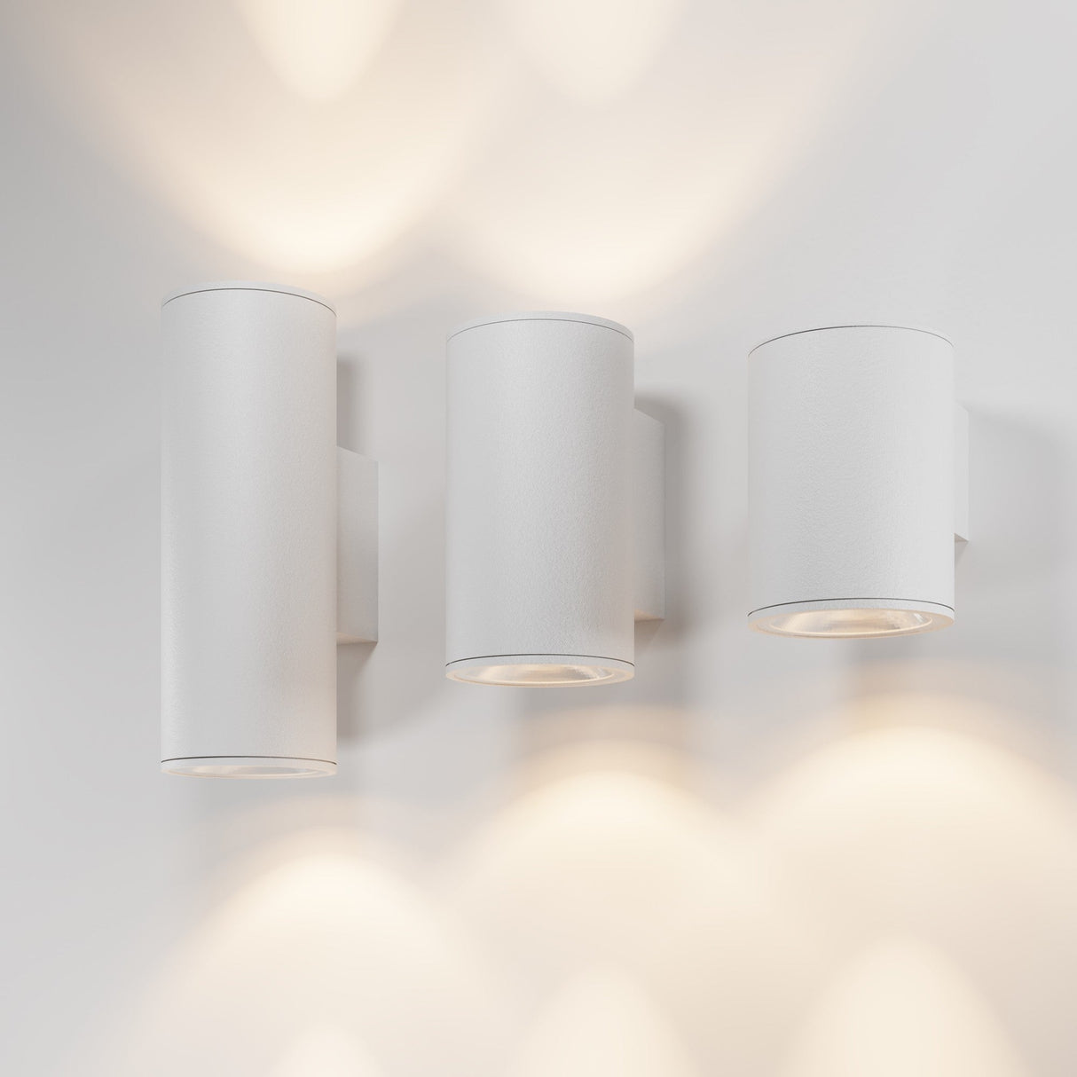 Three Shim Outdoor Wall Light fixtures, each emitting a warm 3000K glow with an IP65 rating, create overlapping light patterns on a white wall. These modern, minimalist cylindrical sconces are evenly spaced to enhance the ambient atmosphere.