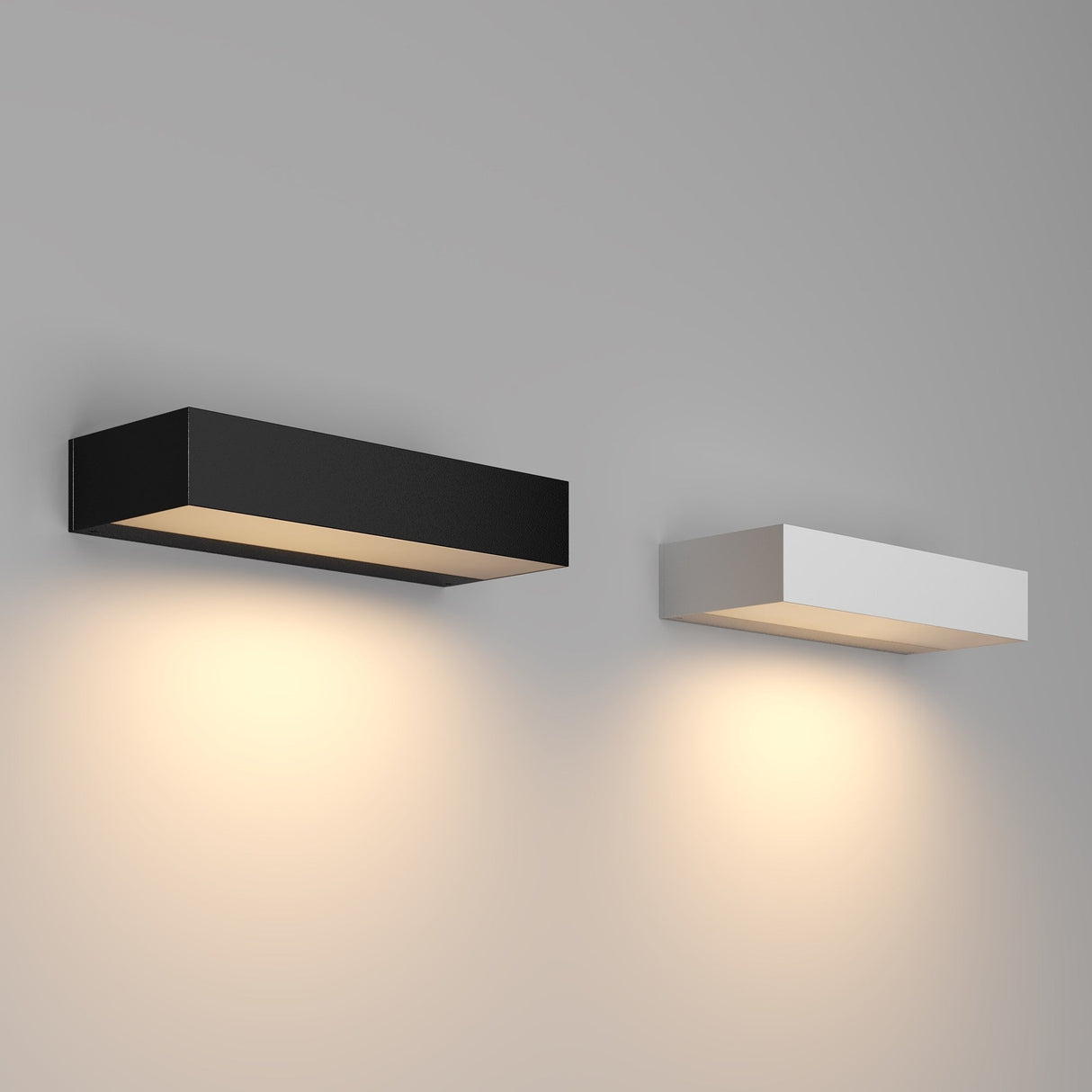 Two modern Lot Outdoor LED Wall Lights, 10W 3000K, are mounted on a gray wall. The left sconce, in graphite finish, and the right one, in white finish both emit a warm light that beautifully illuminates the area beneath them. Ideal as corrosion-resistant outdoor lighting.