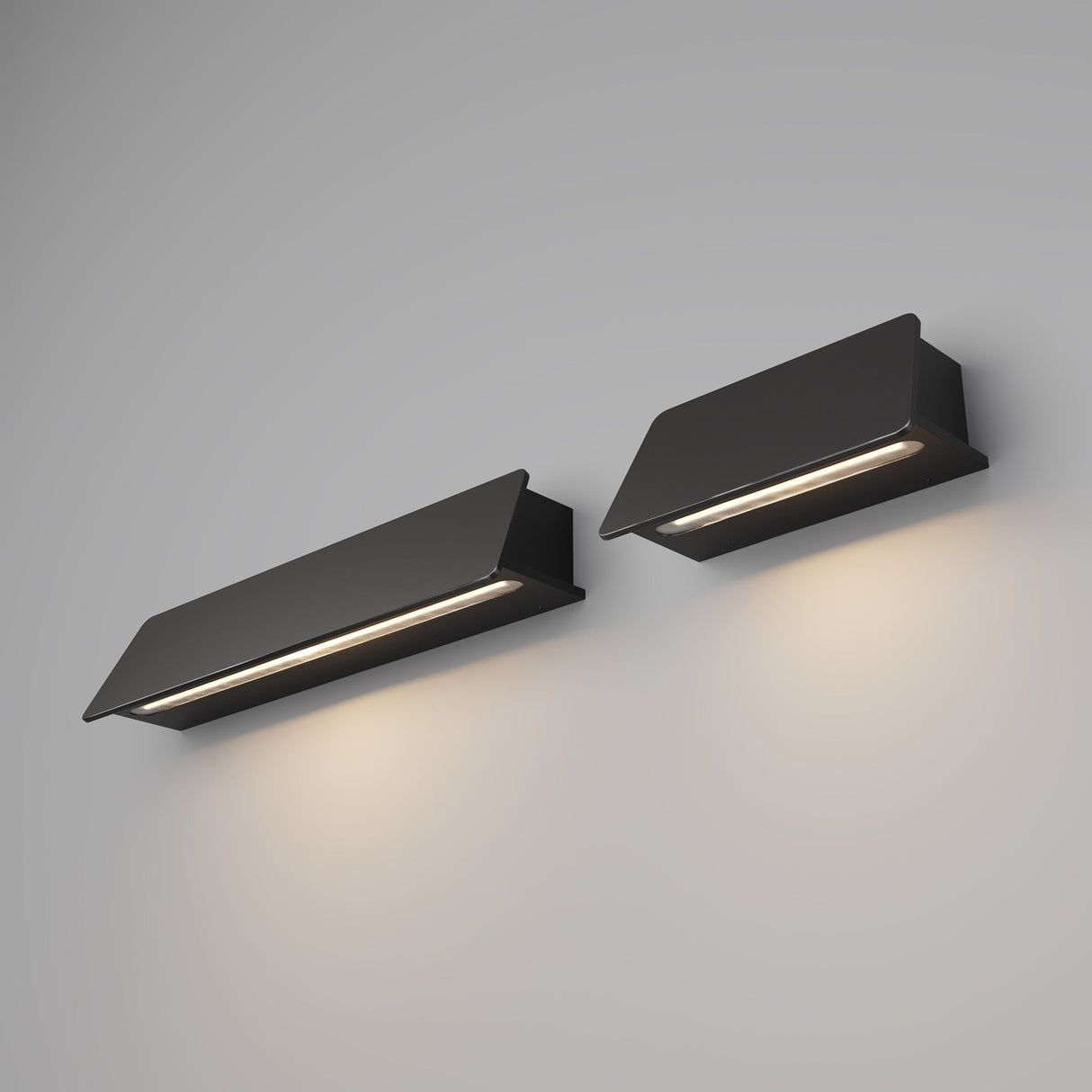 Two Trupp Outdoor Wall Light 6W 3000K sconces in graphite, with a minimalist rectangular design and IP54 rating, are mounted on a light gray wall. They emit a soft downward glow, creating a warm ambiance with their sleek angled tops and flat bases.
