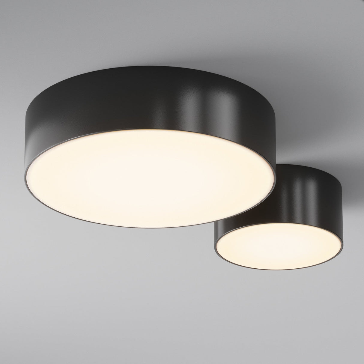 Two Zon Outdoor Ceiling Lights, featuring sleek black cylindrical frames with an IP65 rating, emit a soft, even glow against a light gray ceiling. The larger light is on the left while the smaller one is on the right, both showcasing their refined black finish.
