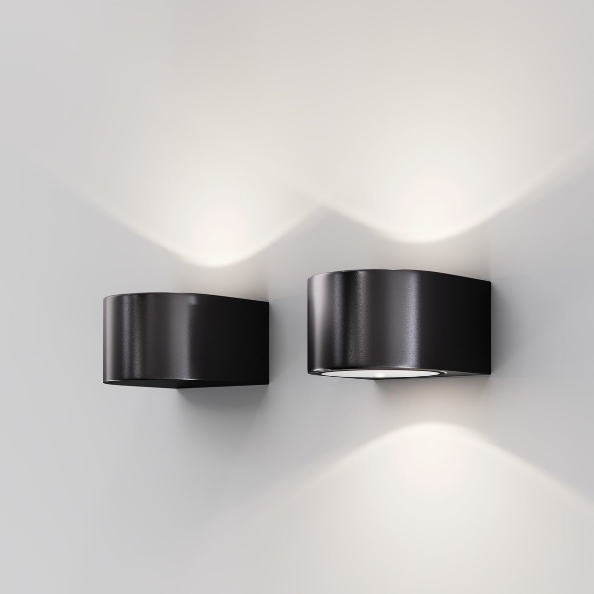 Mounted on a light gray wall, two Blow Outdoor LED Wall Lights in graphite emit soft white LED light both upwards and downwards, casting a symmetrical and energy-efficient light pattern.
