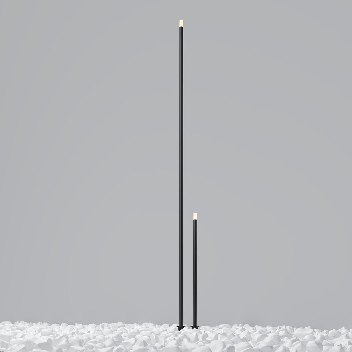 Two sleek, black vertical poles resembling Spear Outdoor Small Spike Light 3000K 1W - Graphite of different heights are set among scattered white pebbles on a light gray background. With IP65 weather resistance, these lights are perfect for any outdoor setting.