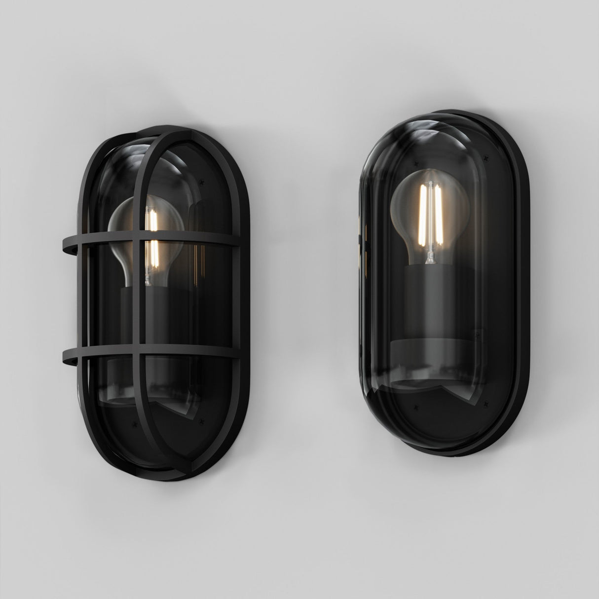 Two modern Candle Outdoor Wall Lights in graphite with transparent glass covers are mounted on a white wall. One light features a protective metal cage and offers IP65 protection for outdoor use, showcasing a contemporary loft-style design with visible bulbs inside.