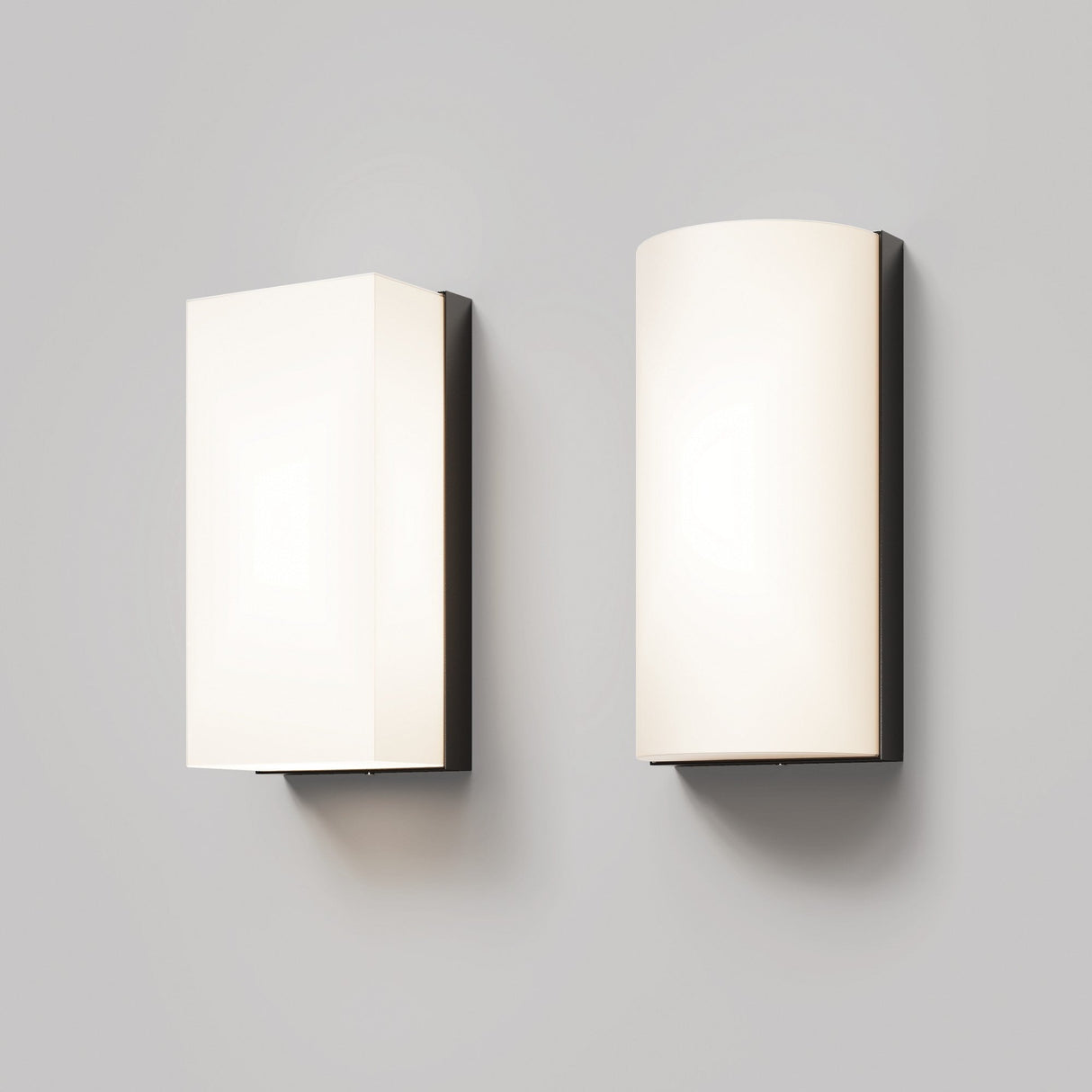 A Badd Outdoor Rounded Wall Light 3000K in graphite is mounted on a light gray wall. Paired with a rectangular LED sconce, both emit a soft glow, creating a minimalist and contemporary aesthetic.