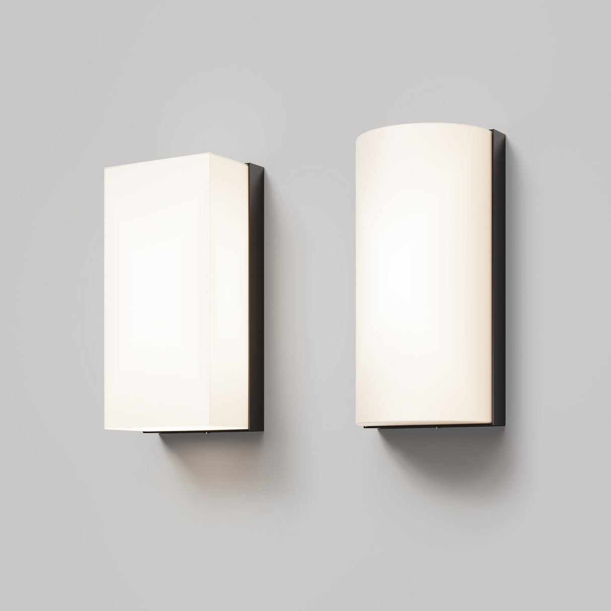 A modern graphite-finished Badd Outdoor Square Wall Light (3000K) is mounted against a light gray background, alongside a curved sconce. Both emit a soft, warm glow using energy-efficient LEDs.
