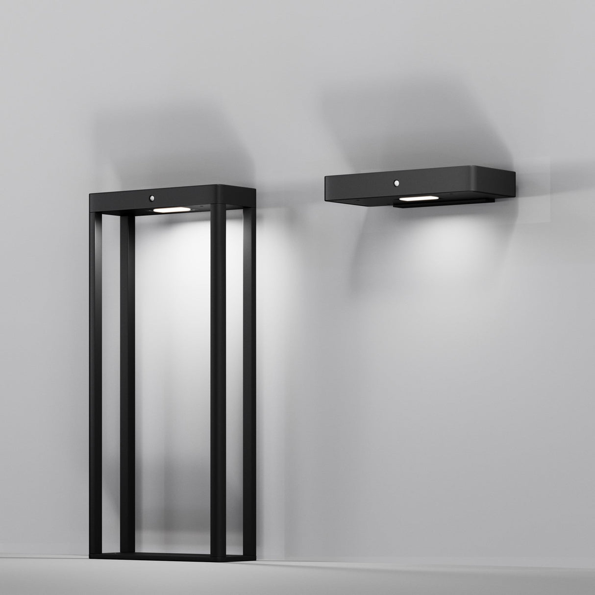 The Pir Outdoor LED Wall Light 3000K in graphite, with its minimalist design, elegantly illuminates against a plain gray background. One light features an open rectangular frame, and the other is solid and compact, both offering soft white solar energy lighting.