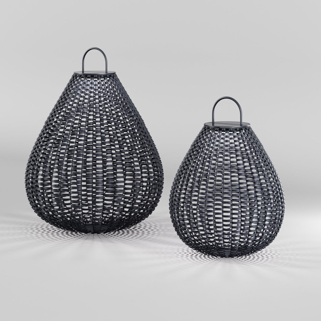 Two decorative, teardrop-shaped Plet Pedestal Light 61cm baskets made of black rattan sit side by side on a light gray surface. Each basket features a loop handle for carrying, with their shadows cast below.