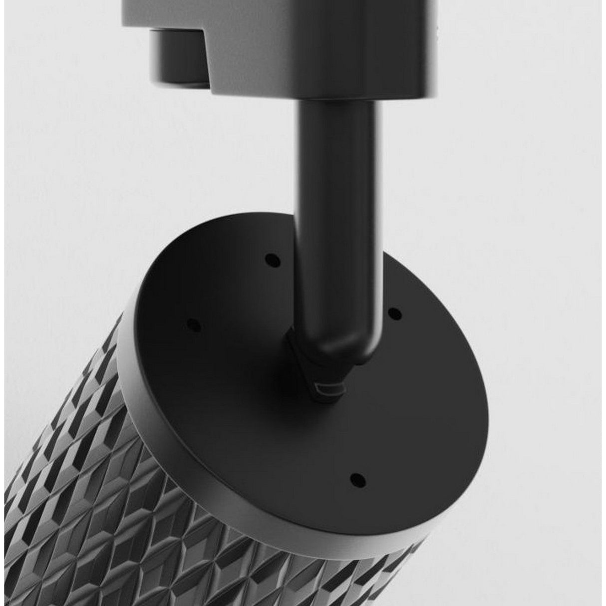 Close-up of the Focus Design Single Phase Unity Track Spotlight - Black featuring a textured, cylindrical metal surface similar to a GU10 base, attached to a flat, round black plate with holes. The gray background accentuates this industrial components intricate details.