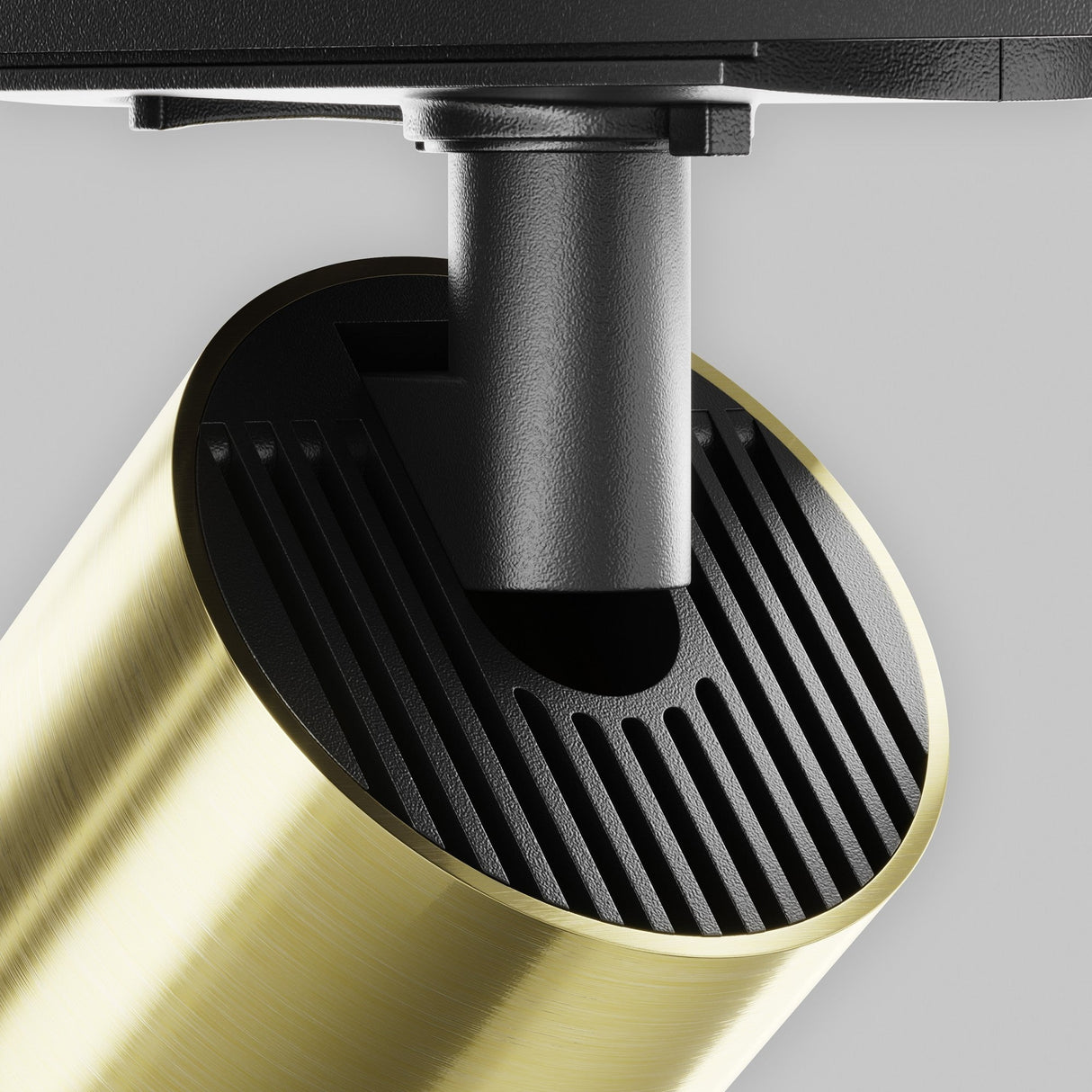 A close-up of the Focus LED Single Phase Unity Track Spotlight features a gold brass cylindrical shade, textured with fine lines for a wide beam angle. A black rod connects to the ceiling mount, highlighting a black louvered detail at the brass shades opening.