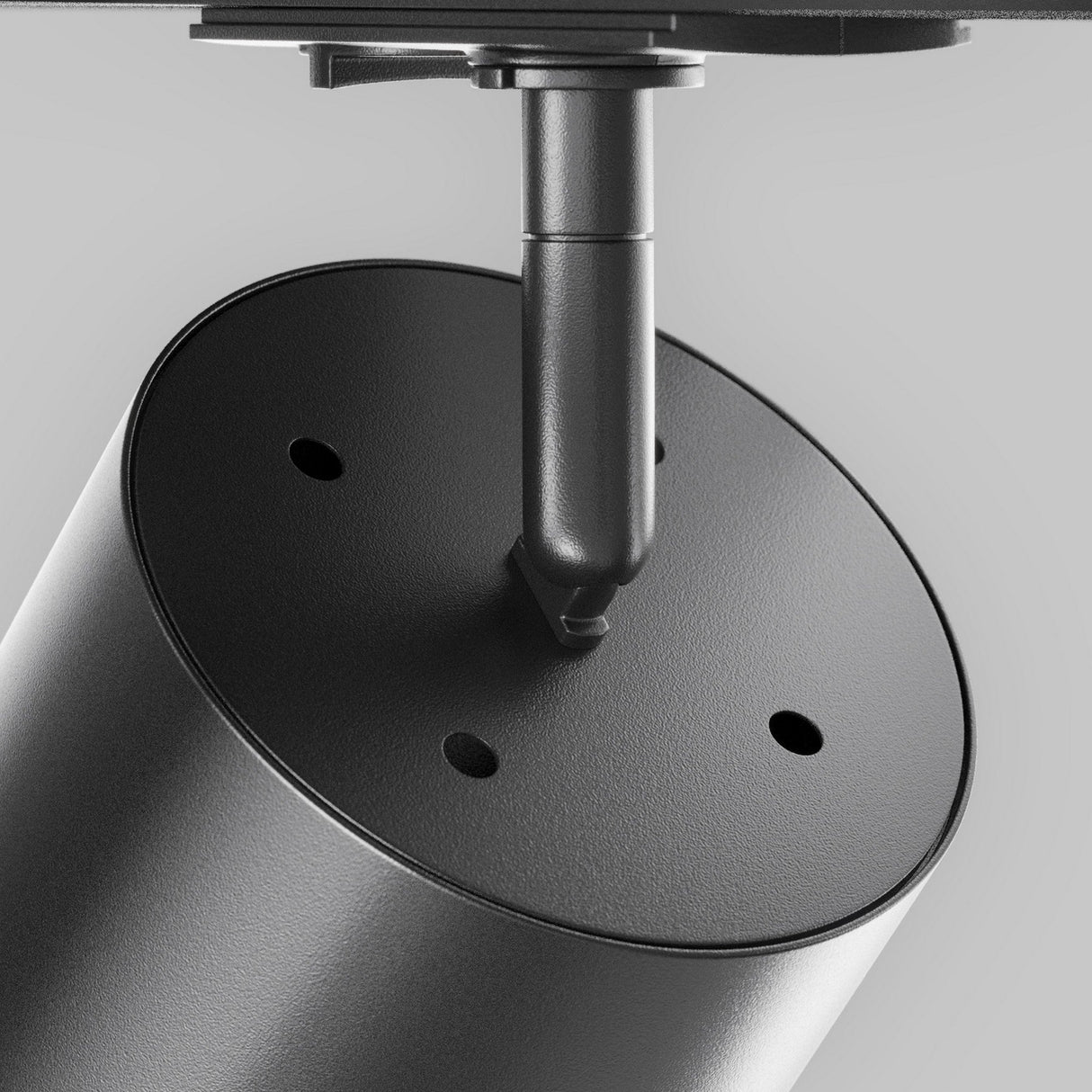 A close-up of the Polar LED Single Phase Unity Track Spotlight in black, featuring a cylindrical design with three circular openings, mounted on a thin vertical rod under a flat surface. The neutral gray background enhances its sleek accent lighting appeal.