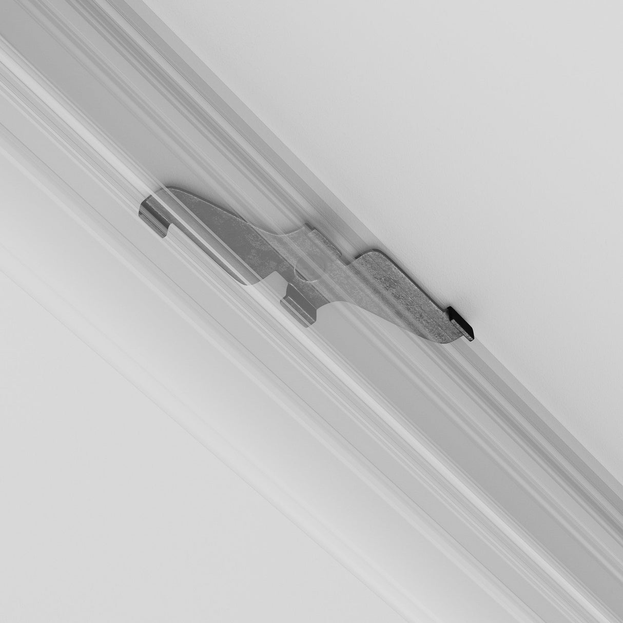 A black Exility Magnetic Track Clamp is mounted on a well-lit white ceiling. It extends horizontally with a curved design secured between two parallel ridges, perfectly complementing the ceilings smooth surface for an elegant appearance.