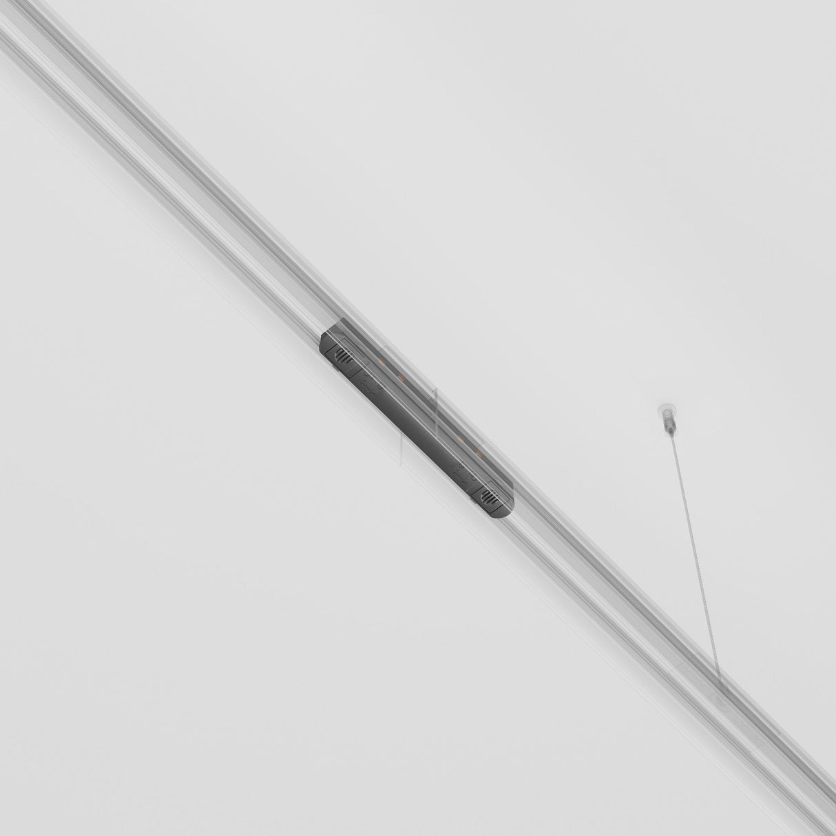 The Exility Track Straight Power Connector - Black features a sleek, minimalistic design with a slender cylindrical shape and central black section. Integrated into a track lighting system, it hangs diagonally from thin wires against a plain white ceiling.