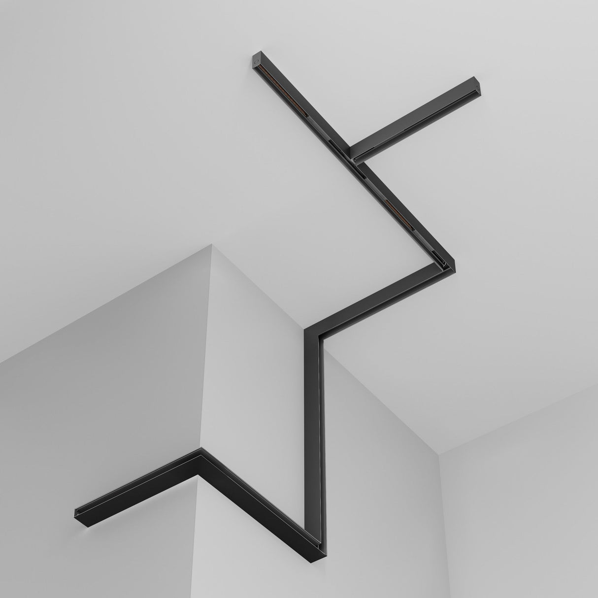 The Exility Magnetic Surface-Mounted Track 2m - Black is installed in a zigzag pattern along the white corner wall and ceiling, forming a geometric design. This customizable light fixture creates subtle shadows that enhance the rooms minimalist aesthetic.