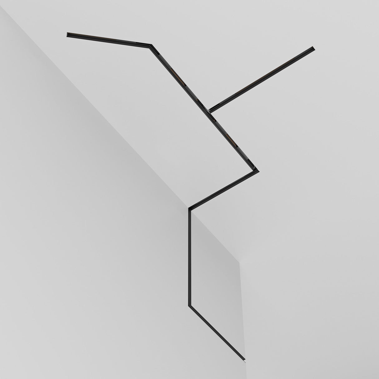 The Exility Magnetic Recessed Track 1m for Plasterboard 9.5mm in black forms sharp geometric shapes on white walls and ceilings, creating a modern minimalist look. Integrating this recessed magnetic track lighting enhances the sleek aesthetic with its seamless 48V system, ideal for contemporary spaces.