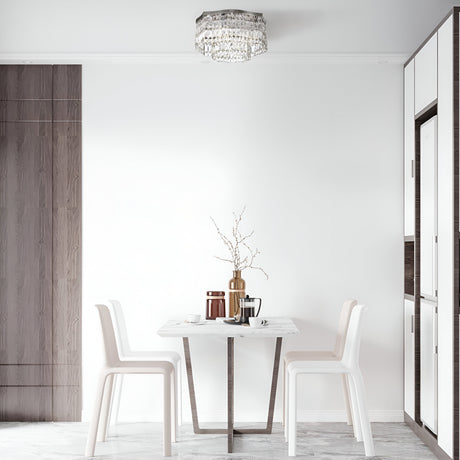 A minimalist dining area features a small table set for two, white chairs, a marble tabletop, and the elegant Dune 6 Light Flush - Chrome & Crystal above. A gold vase with delicate branches serves as a centerpiece against a white wall with wooden accents.