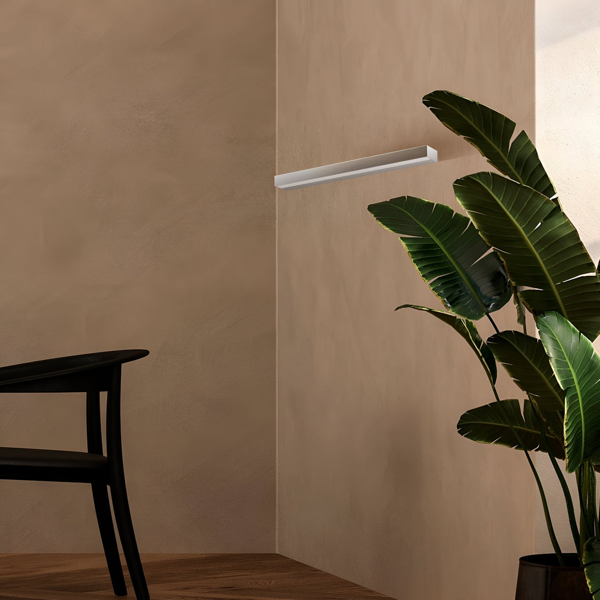 A minimalist interior includes a wooden chair, potted plant, and an Orion LED Picture Light 9W 4000K. This sleek, energy-efficient fixture enhances the beige walls and wooden flooring, adding a warm, modern atmosphere with silver and white elegance.