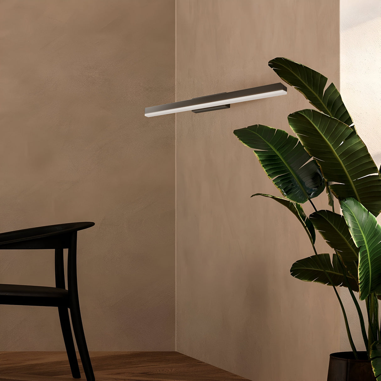 A minimalistic room features a modern black chair, a sleek wall-mounted shelf lit by the Fichte LED Picture Light 14W 4000K, and a tall green plant in the corner. Beige walls and wooden flooring complement the lighting for a warm, contemporary ambiance.