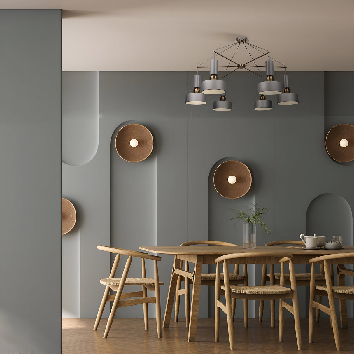 A modern dining room features a round wooden table with matching chairs, gray walls with circular recessed lights, and the Void 6 Light Chandelier - Grey overhead. A small plant on the table completes the sleek modern design.