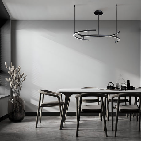 A modern dining room with a minimalist design includes a sleek table, four chairs, and tall dried plants in a vase. The Line LED Circular Suspension 3000K - Black light, adjustable in height, illuminates the space with muted tones and natural light from a nearby window.