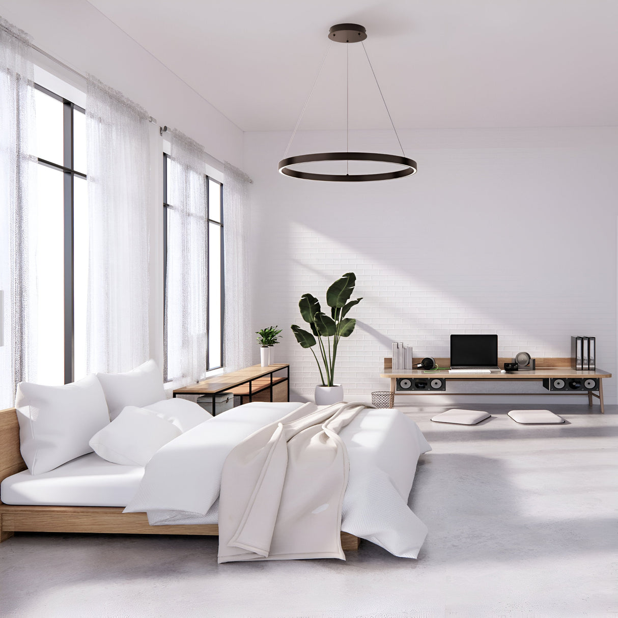 A minimalist bedroom includes a low wooden bed with white bedding, a wooden desk with a computer and speakers, and a potted plant. Natural light enters through large windows with sheer curtains, while the Rim LED Circular Suspension Light 60cm 4000K - Black efficiently illuminates from above.