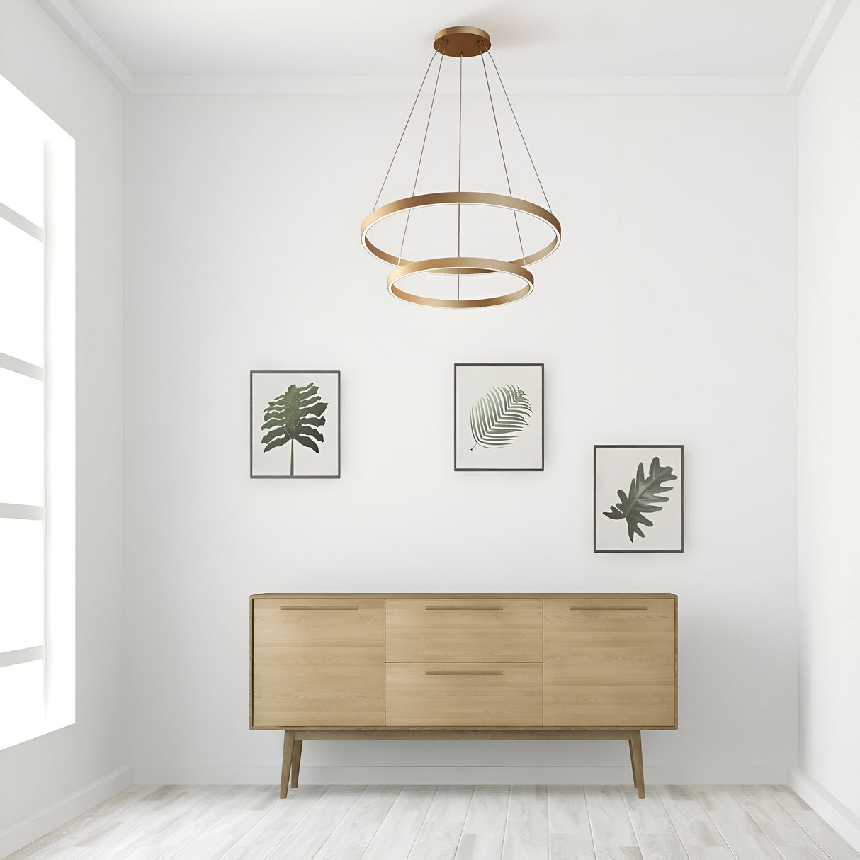 Minimalist room with a wooden sideboard and four framed botanical prints. The Rim LED Double Circular Suspension Light in brass adds elegance to the modern interiors. Neutral tones prevail, with a large window flooding the space with natural light.