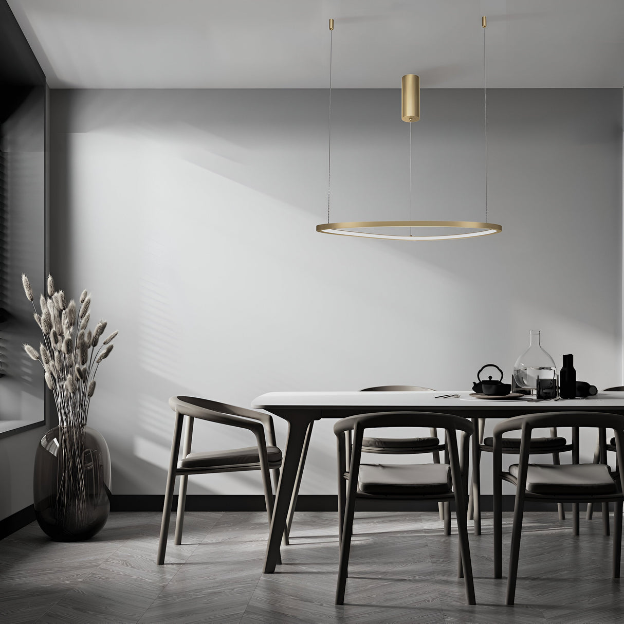 A minimalist dining room boasts luxury with a sleek rectangular table and four chairs. A brass pendant light, the Glint LED Circular Suspension Light 60cm, hangs above. In the corner, a large vase with dried plants accents a glass carafe and teacups on the table.