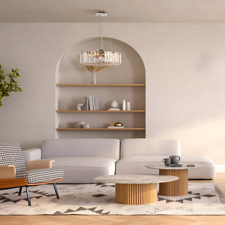 A modern living room features a white sofa, patterned armchair, and round wooden coffee tables on a geometric rug. Decor adorns built-in shelves in an arched alcove. The Recinto 6 Light Chandelier - Chrome illuminates the space, while a small plant adds greenery.