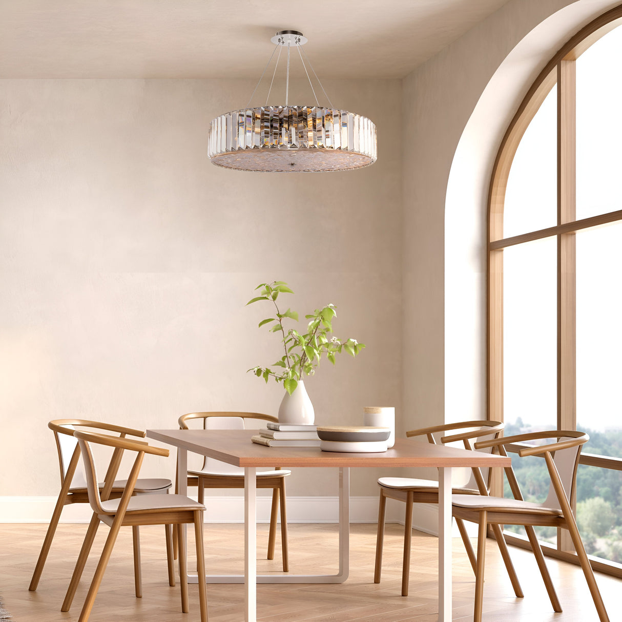 In a modern dining room, a wooden table is surrounded by four chairs. A Recinto 8 Light Chandelier in chrome illuminates crystal plates and a potted plant. Natural light streams through large arched windows, enhancing the serene ambiance.