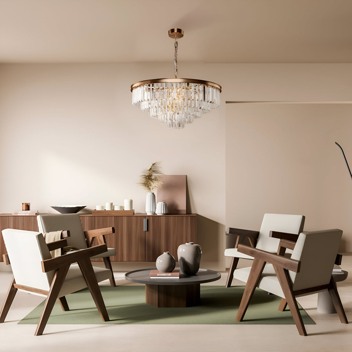 Minimalist living room features modern wooden chairs and a round table on a green rug. A wooden cabinet with decor items accents the back wall. The ceiling showcases the Revero 12 Light Chandelier - Brass, with crystal pendants, casting a warm, inviting glow.
