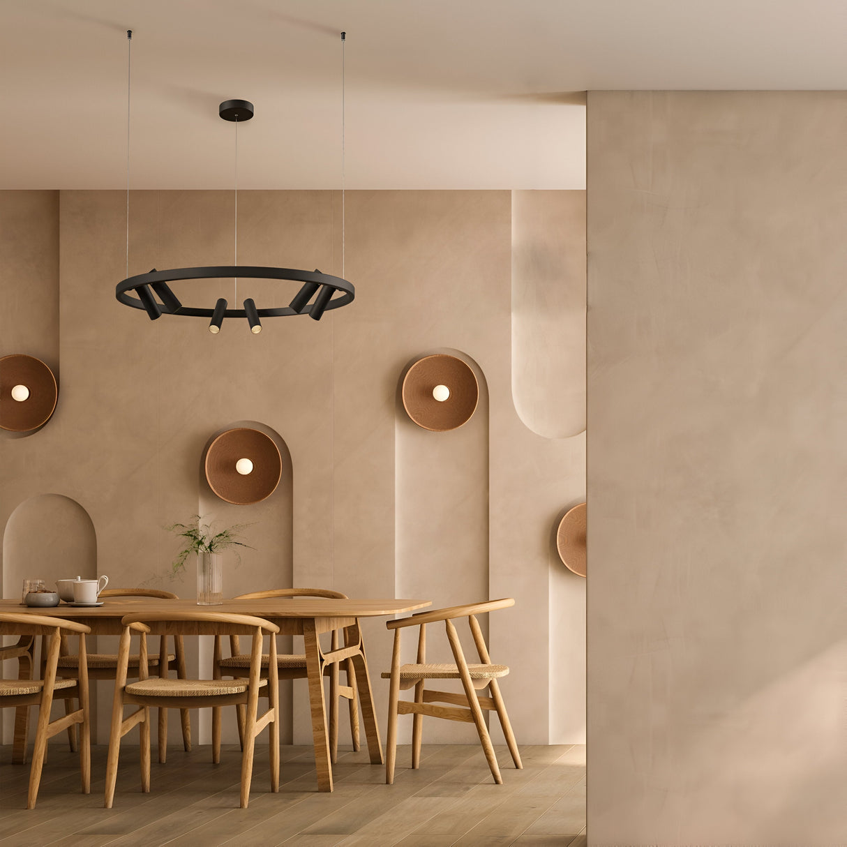 A modern dining room features a wooden table with six chairs. Suspended above is the black Satellite LED Circular Suspension Light, enhancing the industrial-style decor. The walls have a textured beige finish with decorative circular indents and soft lighting, while a flower vase adorns the table.