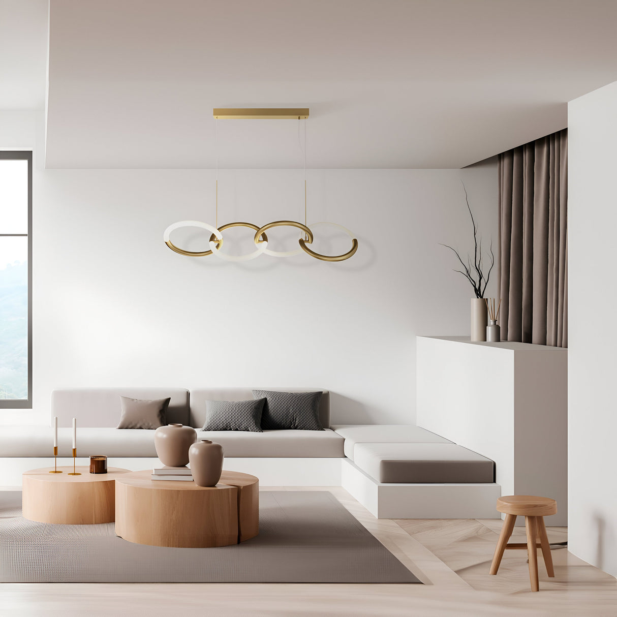 A minimalist living room features a white sofa with gray cushions and a wooden round coffee table. The Node LED 4 Rings Linear Suspension Light in gold enhances the ambiance. Beige curtains drape ceiling-high, paired with decorative vases and a small floor stool.