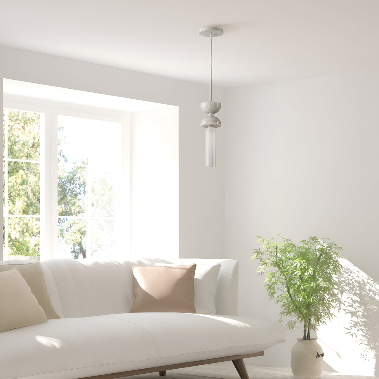 A minimalist living room is accentuated by a white sofa, beige cushion, and the Kyoto Pendant Light in White with a White Marble Base. Sunlight floods through large windows, illuminating a potted plant on the floor and enhancing the serene, bright ambiance.