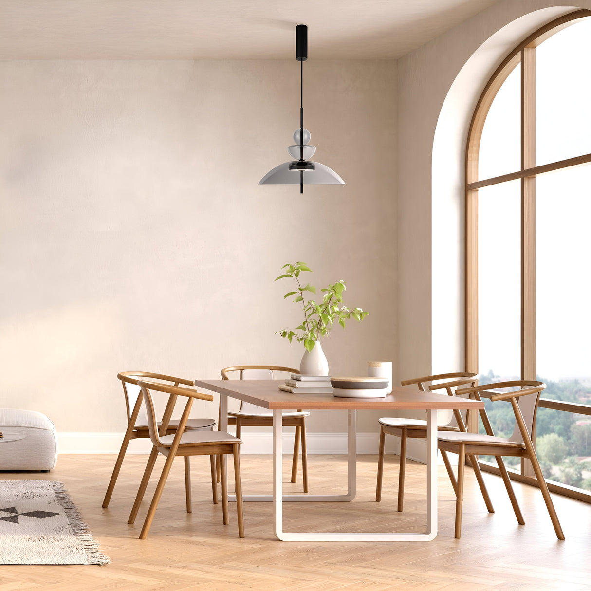 A minimalist dining area showcases a rectangular wooden table, four matching chairs, and a potted plant centerpiece. The space is lit by the Bangkok LED Pendant Light 40cm in black with a grey glass shade, while large arched windows flood the area with natural light.