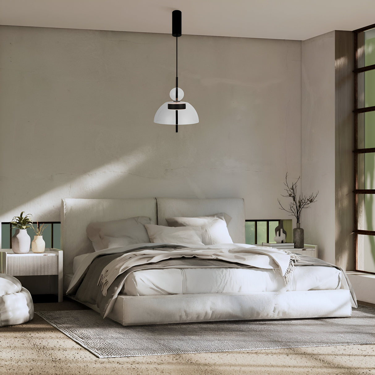 A modern bedroom has a large bed with white linens illuminated by a Bangkok LED Pendant Light 25cm - Black With Round Clear Glass Shade. A black metal fixture hangs above, and to the right, vases and a plant sit on a nightstand. Sunlight streams through tall windows, casting shadows on the walls.