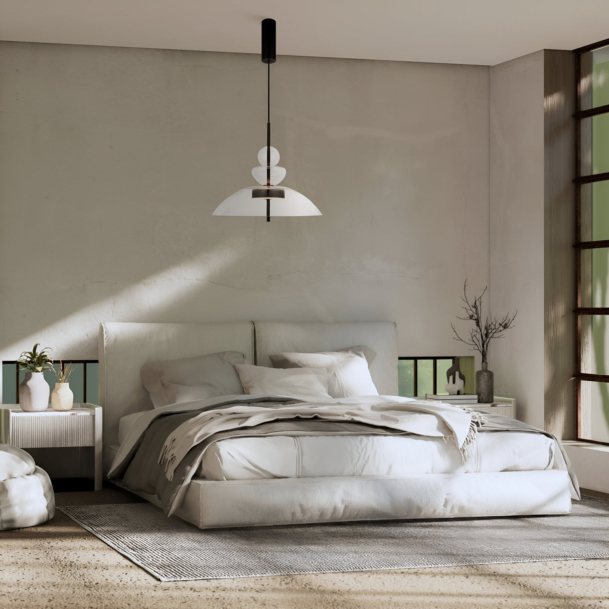 A minimalist bedroom features a large bed with white bedding and pillows, flanked by two decorative nightstands. The Bangkok LED Pendant Light 40cm in black with a transparent glass shade hangs above. Sunlight pours through a large right-side window, enhancing the modern design.