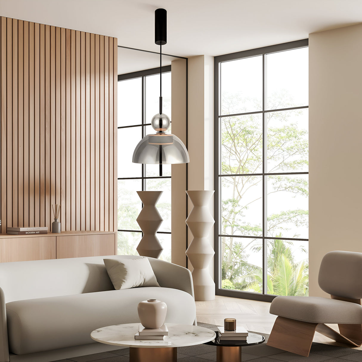 A modern living room features a light gray sofa, round marble coffee table with a vase, wooden accent wall, and large windows showcasing trees. The Bangkok LED Pendant Light 25cm in Black with Round Smoky Glass Shade hangs above, enhancing the elegance of the contemporary gray chair.