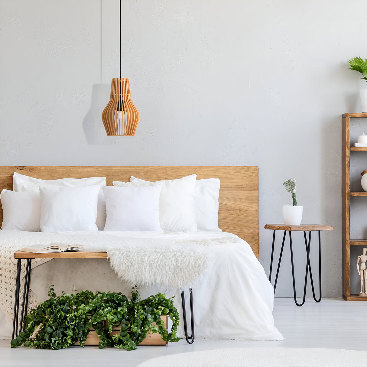 A serene bedroom features a wooden bed frame with white bedding from the Modern Nature collection. A wooden bench with greenery sits at the foot of the bed, while a Roots Pendant Light (20cm Black with Beige Wooden Cone Dome Shade) hangs above. A plant table and decor shelving unit complete the minimalist look.