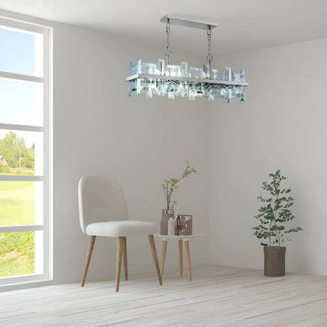 The serene minimalist interior features a Cerezo 8 Light Suspension in Chrome, contemporary décor lighting, a light gray chair, and a small white table with two vases. A potted plant sits on the floor by the window displaying a green landscape. White walls and wood flooring enhance the space.