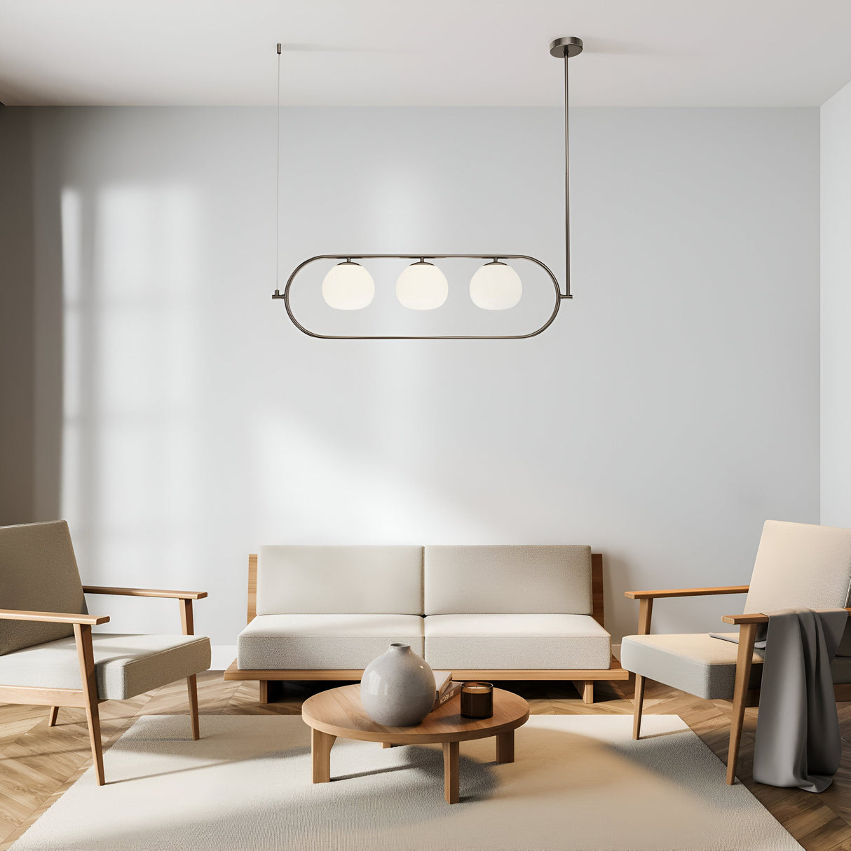 A minimalist living room features beige sofas, a round wooden coffee table with a gray vase, and two matching armchairs. Above, the Erich 3 Light Suspension in nickel with white glass hangs gracefully. The wooden floor is bathed in sunlight streaming from the left.