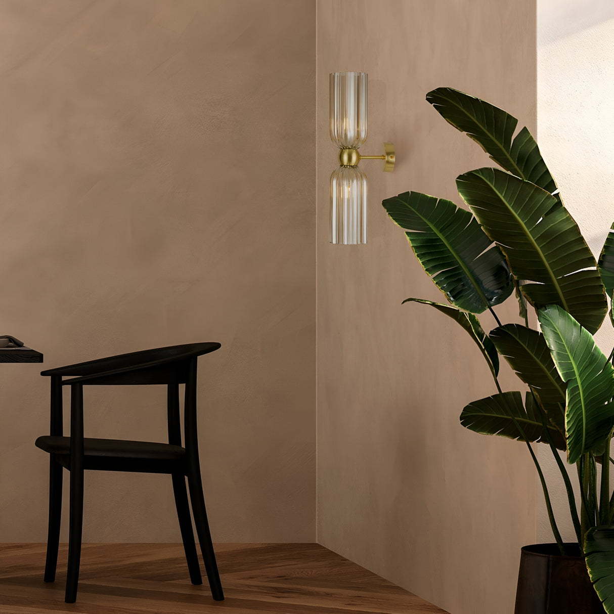 The modern interior includes a black chair and a tall green plant in the corner, illuminated by the Antic 2 Light Wall Light featuring gold and cognac glass, mounted on a beige wall. The parquet floor enhances the minimalistic and well-lit atmosphere.