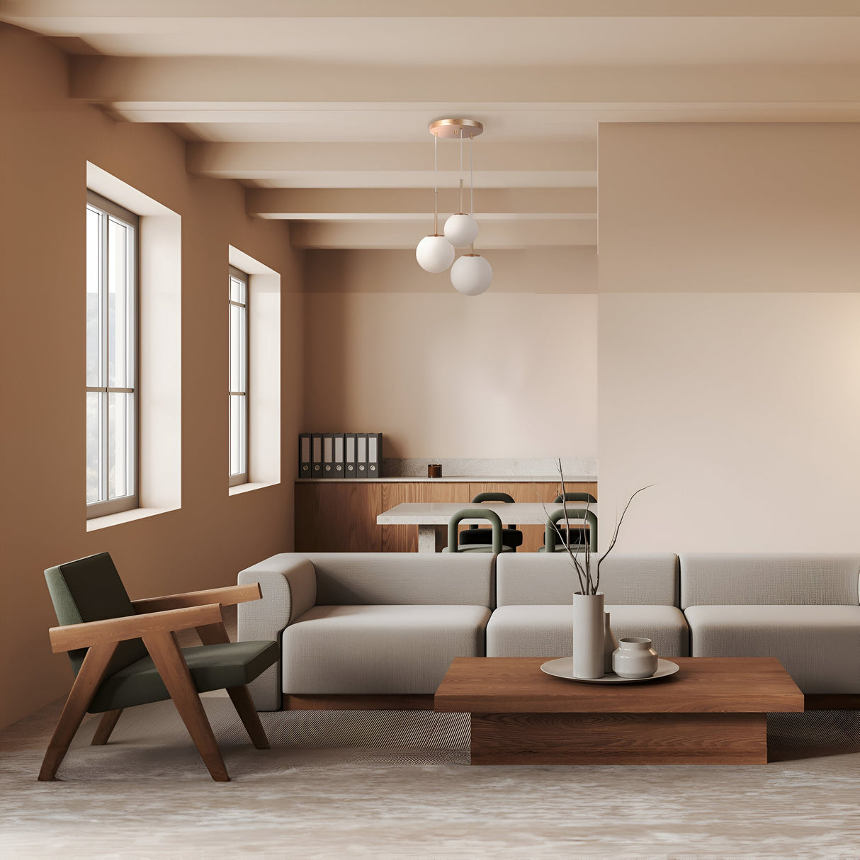 Minimalist elegance defines this living room, with beige walls and a light gray sectional sofa. A wooden coffee table holds a vase of dried branches. A green armchair is by the windows, with a dining area featuring dark chairs in the background, illuminated by the Basic form 3 Light Cluster Pendant - White & Gold.