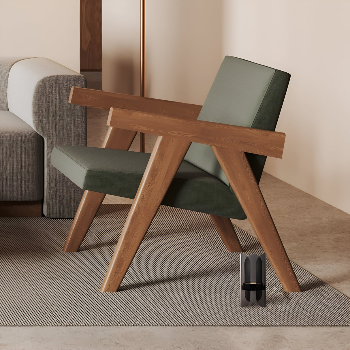 In a modern living room, a wooden armchair with green cushions stands next to a gray sofa under ambient light. The setup rests on a textured gray rug atop a stone floor, complemented by an Insight LED Table Lamp - Black and a small black sculpture near the armchair.