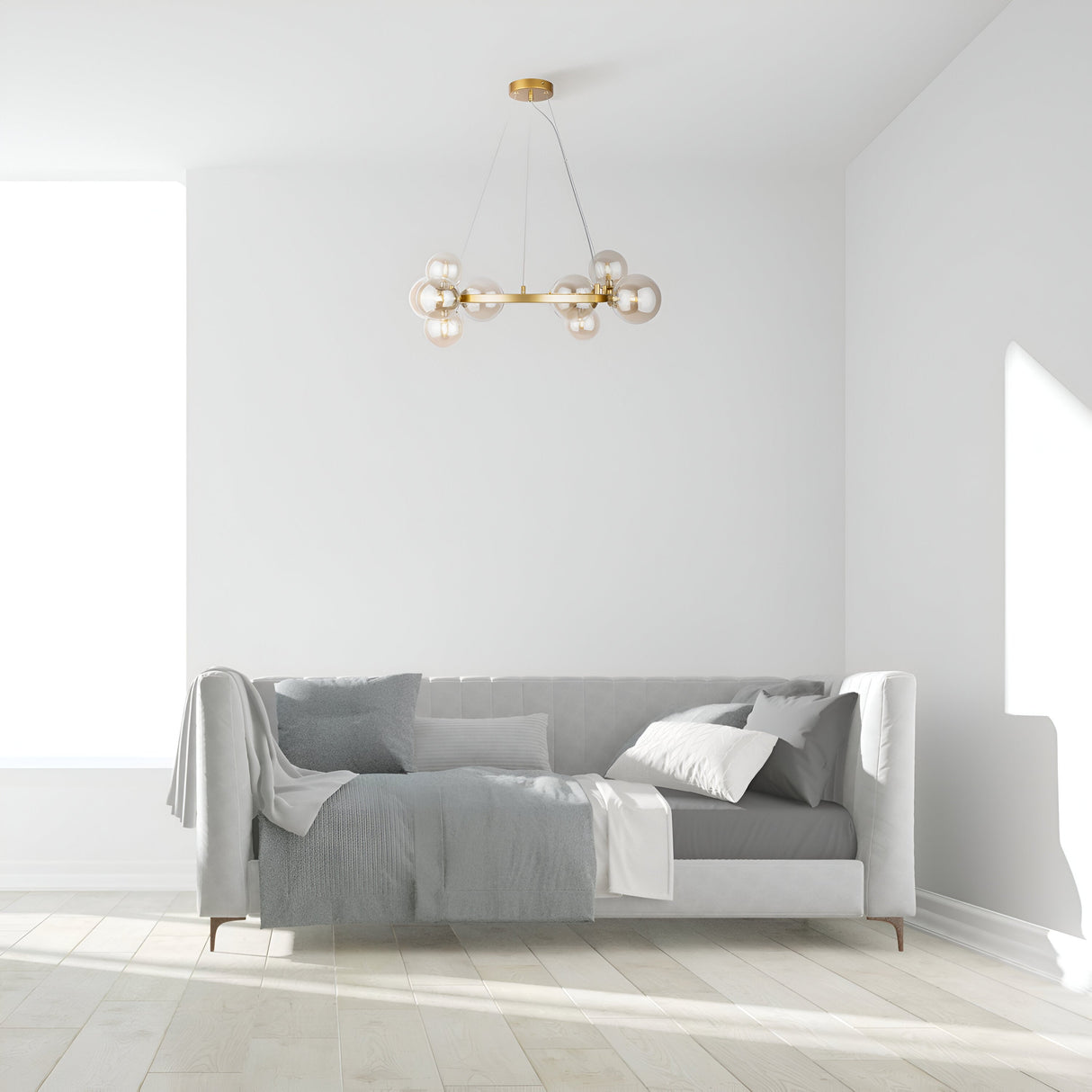 Minimalist living room with a light gray sofa, assorted pillows, and blankets. A modern Dallas 11 Light Suspension in gold with amber glass spheres hangs above. The wooden floor and large window create a bright, airy atmosphere.