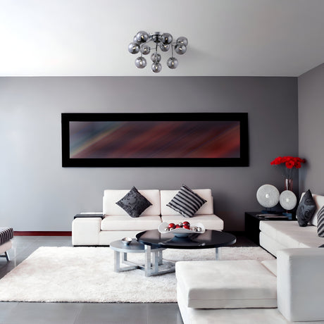A modern living room with gray walls showcases a sleek sofa set with striped and patterned pillows. A long abstract painting hangs above the sofa, while a round coffee table sits on a white rug. The Dallas 12 Light Semi-Flush - Chrome With Smoky Glass fixture adds contemporary flair from the ceiling.