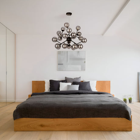 Modern bedroom featuring a wooden bed frame, gray bedding, and multiple pillows. A Dallas 24 Light Chandelier in Black with Smoky Glass adds ambiance above. Minimalistic art adorns the white wall, complementing the light wooden floor and glass closet doors on the left.