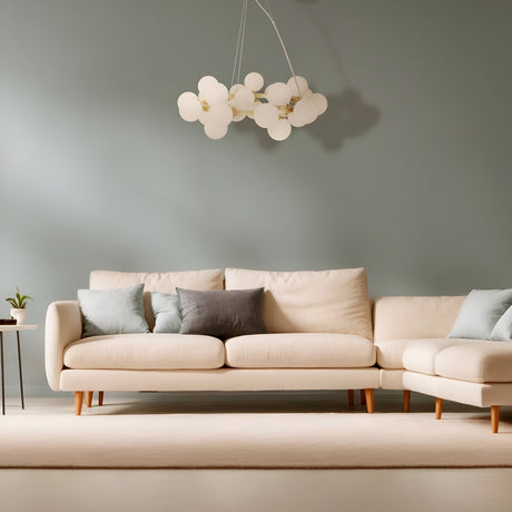 A modern living room exudes elegance with a cream sectional sofa and beige-gray cushions. A Dallas 25 Light Suspension in gold and white adds sophistication, while a small plant on the black side table complements the muted green wall.