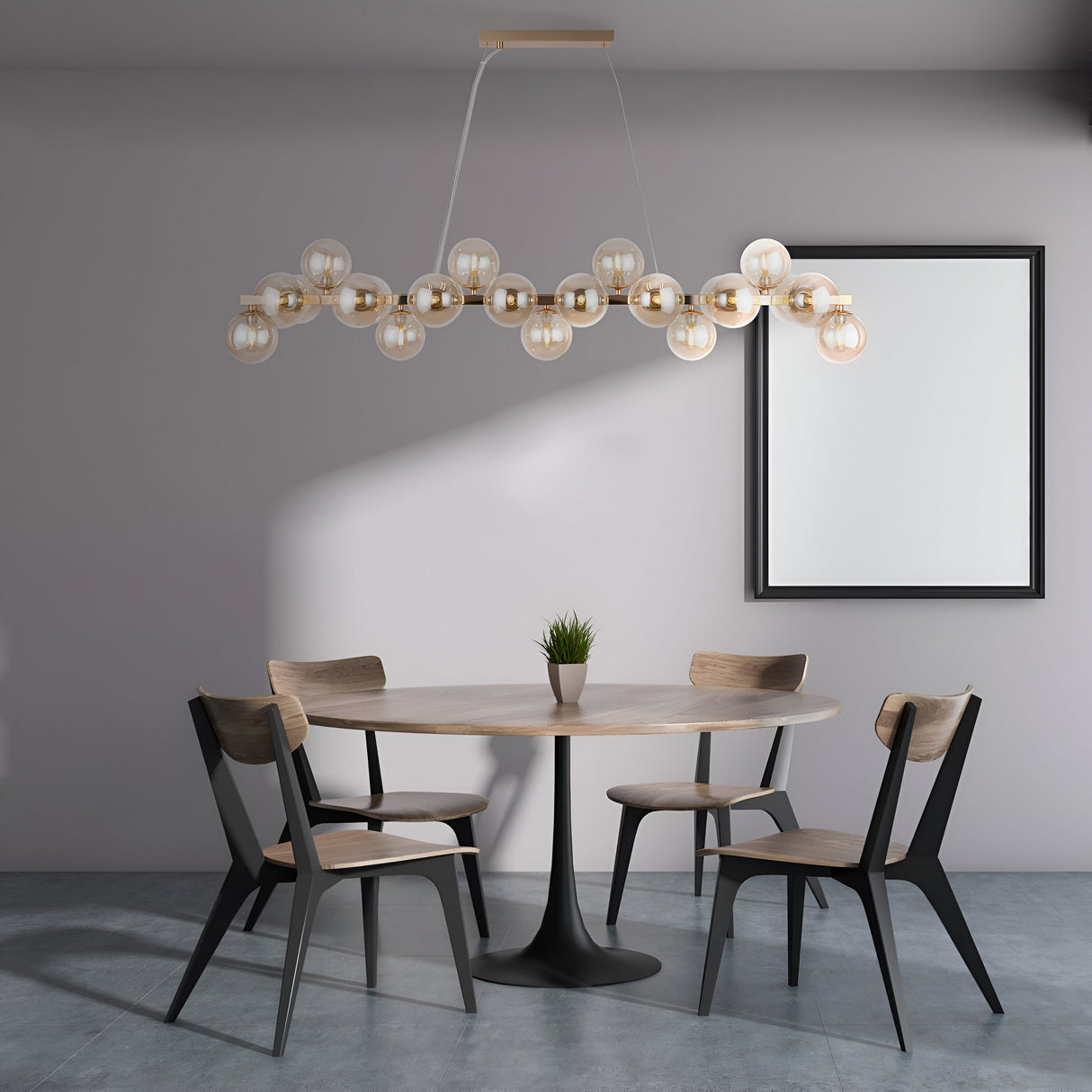 The minimalist dining room showcases a round wooden table with four chairs under the Dallas 25 Light Linear Suspension, featuring gold and amber glass. A small plant decorates the table, complemented by large blank framed wall art against a neutral-toned wall.